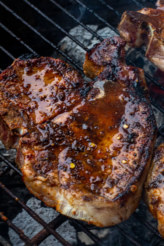 A close up of a glazed pork chop atop the coals in the grill.