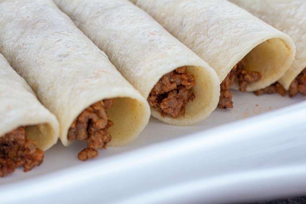 A close up of filled corn tortillas with ground beef filling, prepped for sauce.