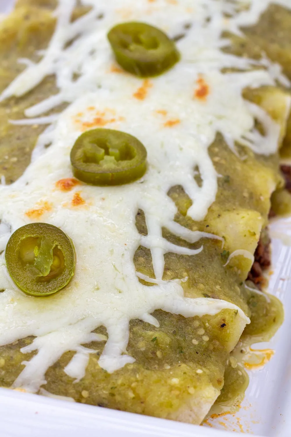 A close up of enchiladas smothered in green tomatillo sauce.