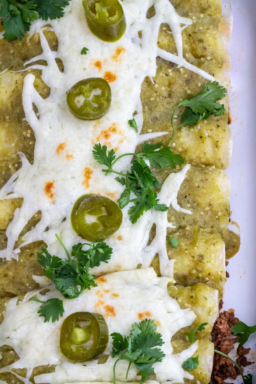 Ground beef enchiladas covered in green enchilada sauce, decorated with jalapenos and cilantro.