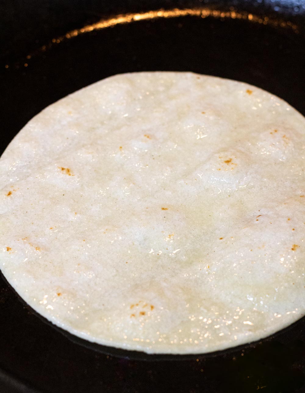 A corn tortilla frying in a cast iron skillet.