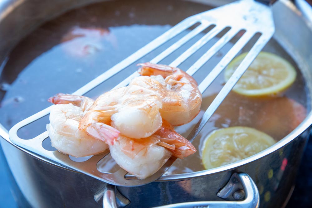 poached shrimp perched on a long spatula above a simmering broth
