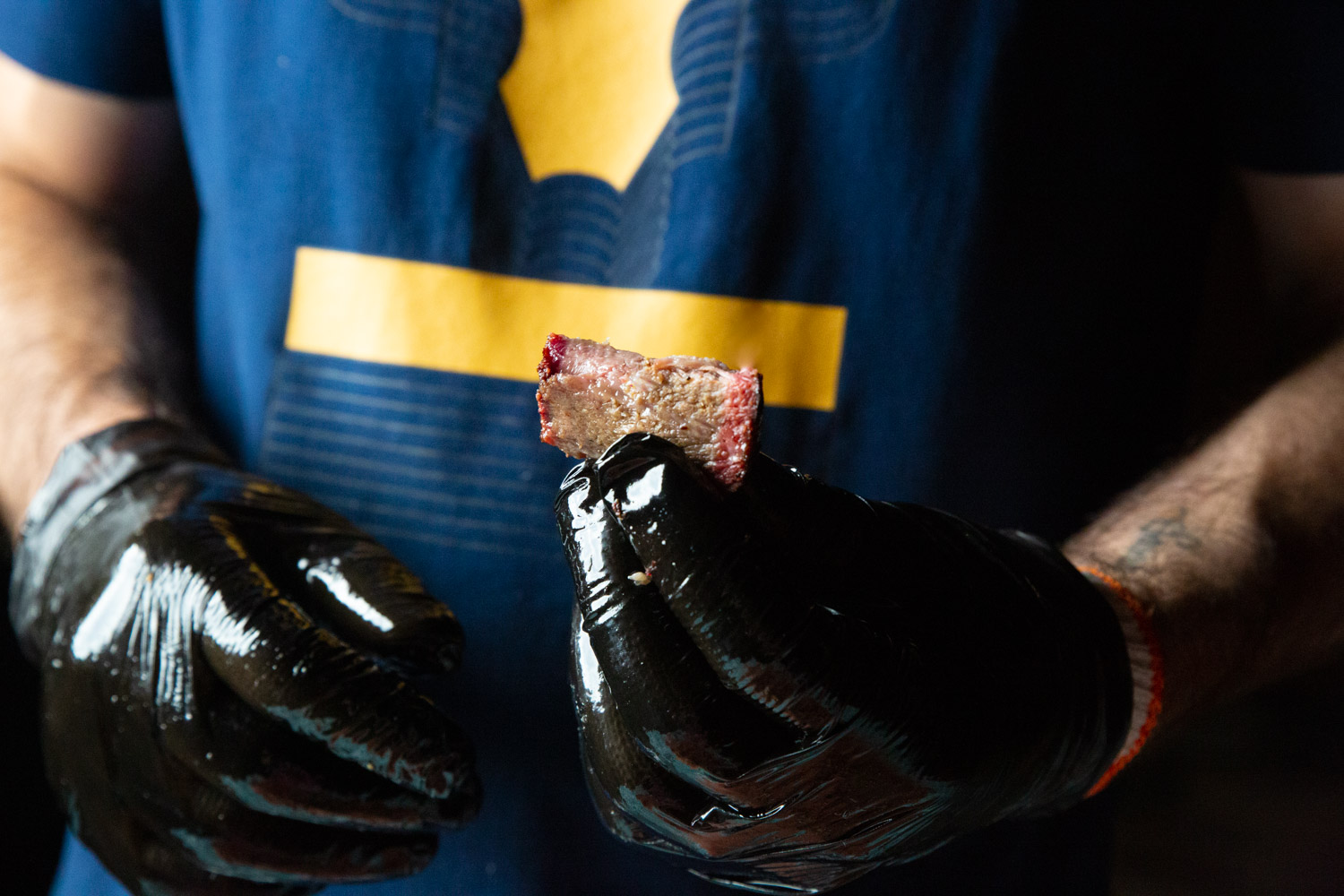 Close up of the pitmaster's black gloved hand holding a perfect slice of smoked chuck roast.