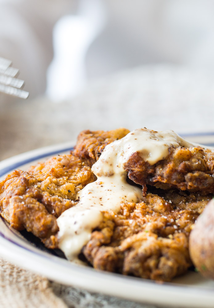 A close up of crunchy, golden chicken fried steak dripping with creamy white gravy.