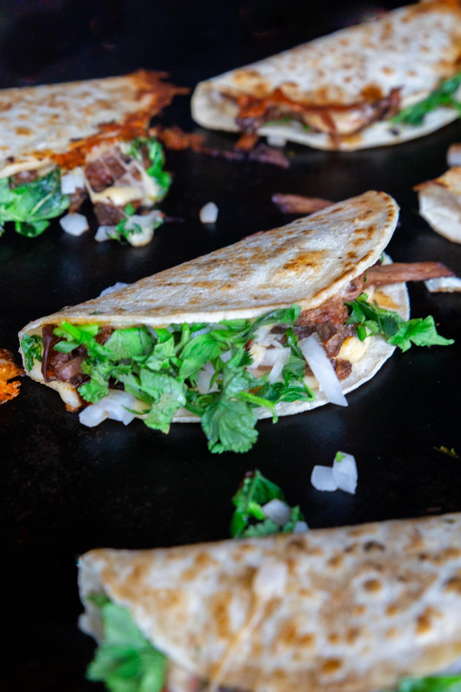 A griddle full of quesabirria tacos frying up.