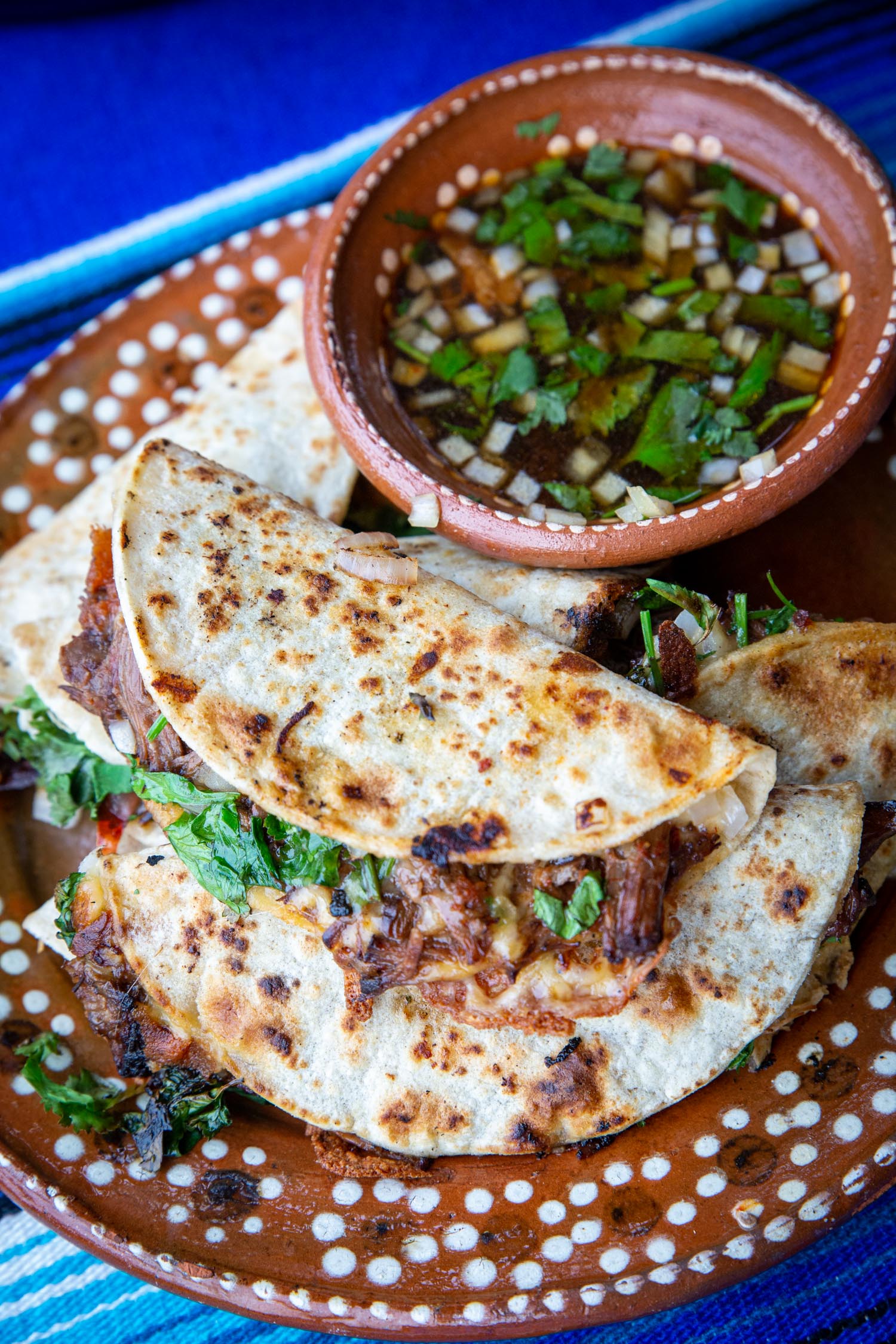 Quesabirria tacos and beef consomme for dipping, on a mexican style plate.