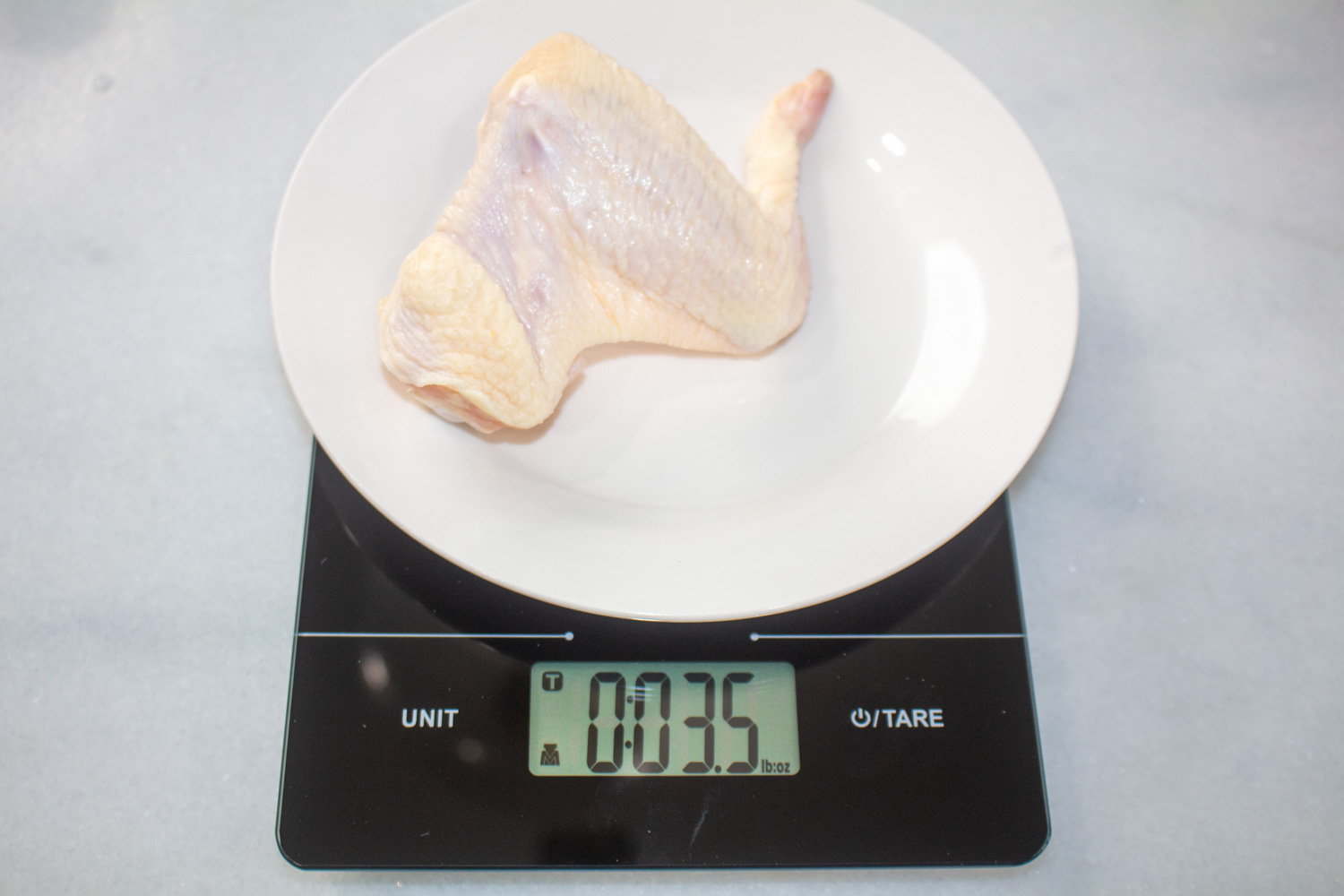 A whole chicken wing on a scale reading 3.5 oz.