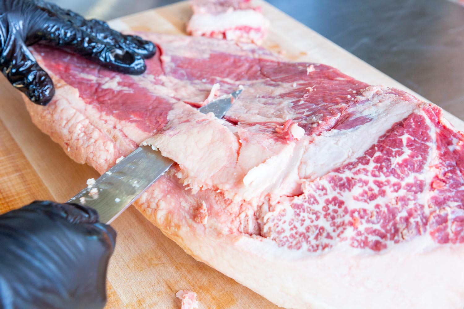 Trimming the top side or meat side of the brisket by removing pockets of fat.