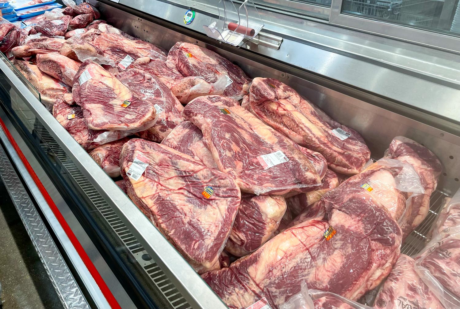 A refrigerated bin at the grocery store full of plastic wrapped briskets, also known as, packer briskets. 