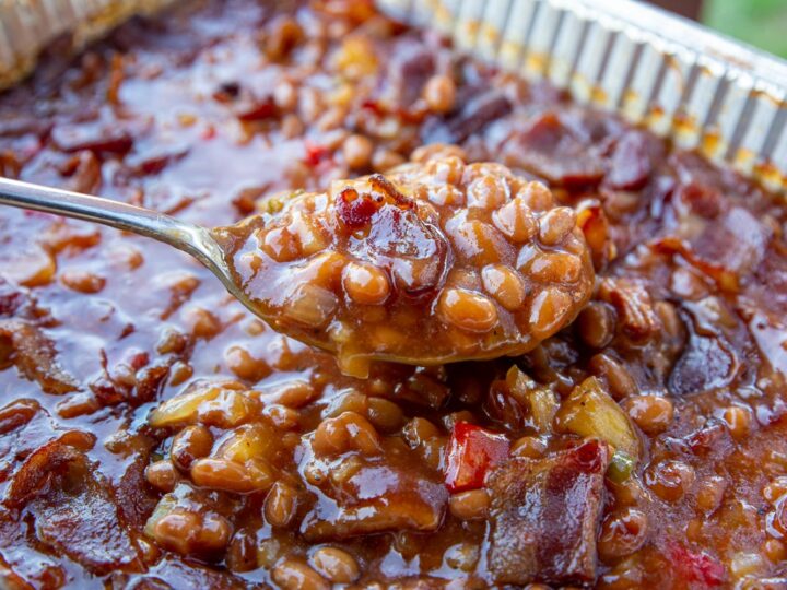 A big pan of smoked baked beans with a spoon holding up a big potion of them.