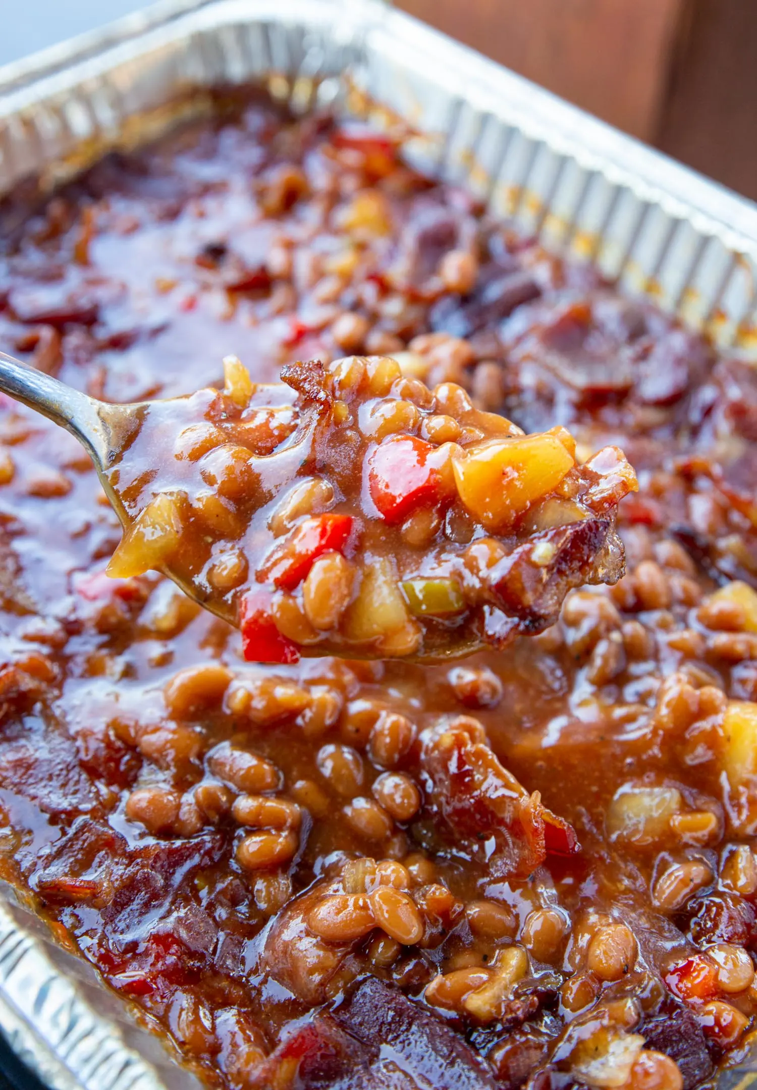 Juicy baked beans served up from a spoon out of an aluminum pan