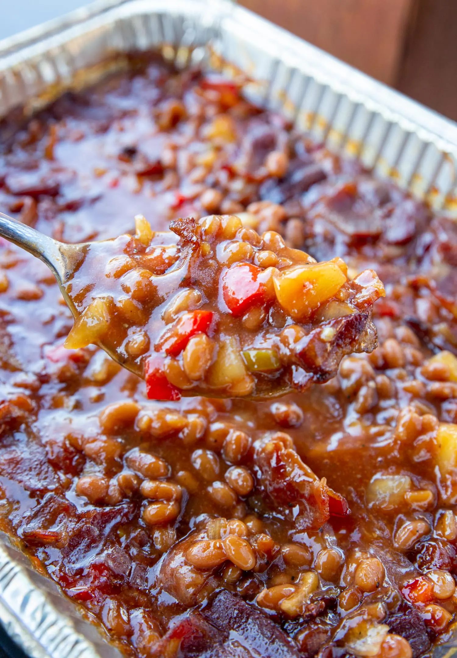 Smoked baked beans served up from a spoon out of an aluminum pan