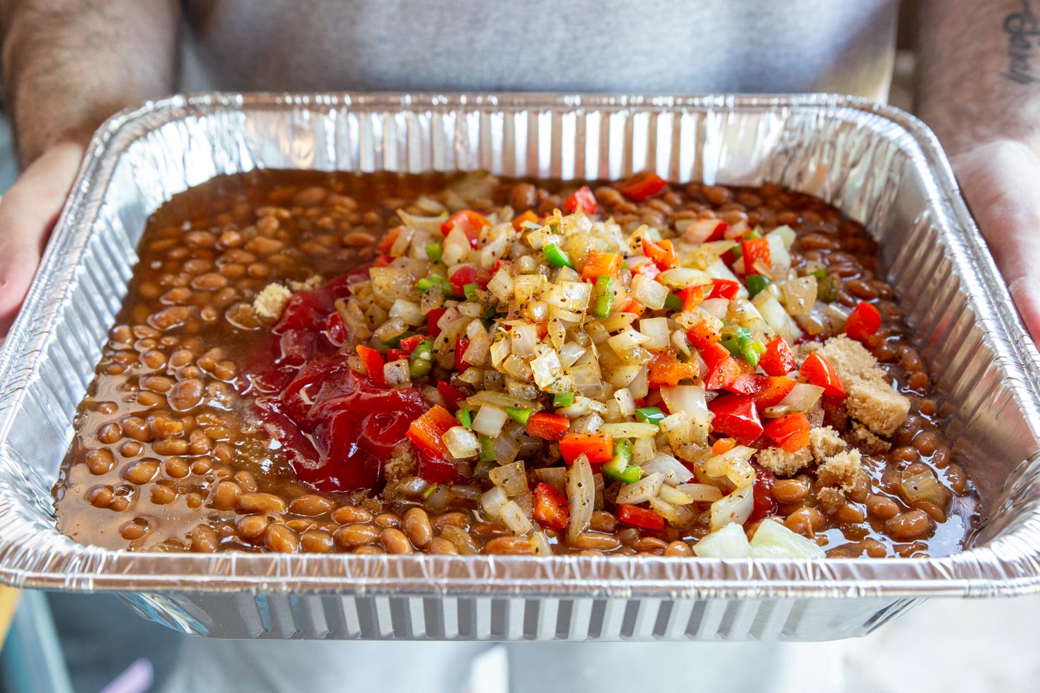 An aluminum pan full of the baked bean ingredients before stirring up