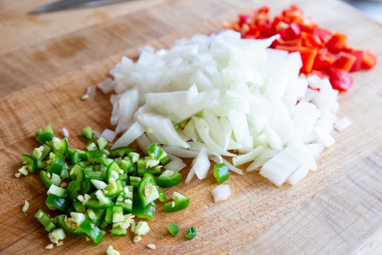 Diced jalapeno, onion, and red bell pepper on a cutting board.