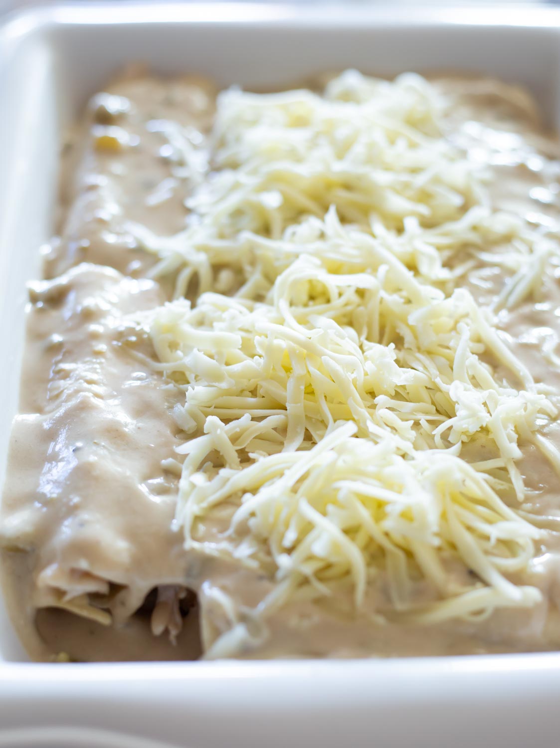 a casserole dish filled with beautiful white sour cream enchiladas topped with cheese