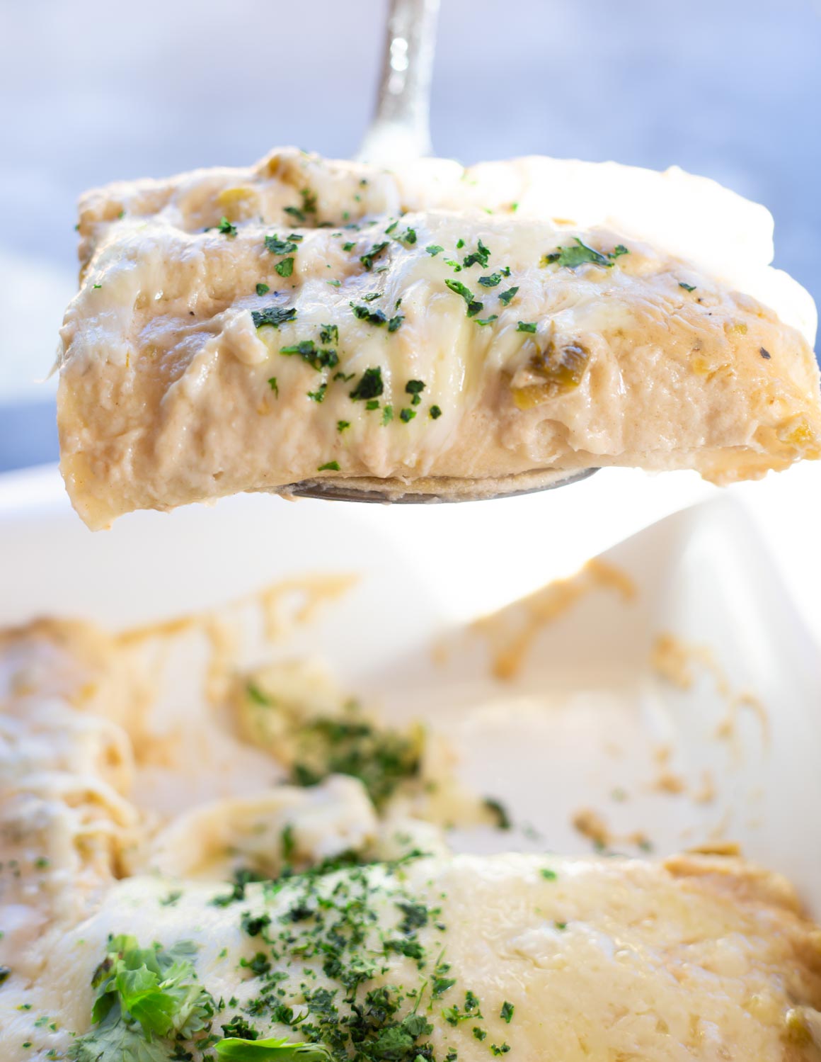 A spatula lifting hot cheesy sour cream enchiladas out of the pan