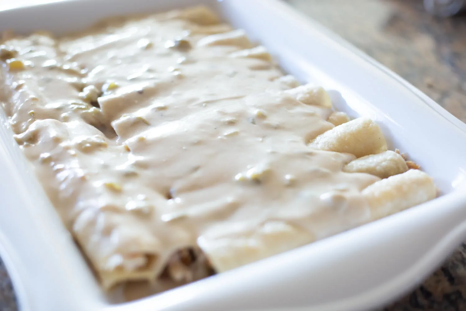 A white casserole dish filled with rolled chicken enchiladas topped with the sour cream sauce.