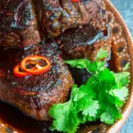 A platter full of steaks topped with mole butter, red peppers, and cilantro