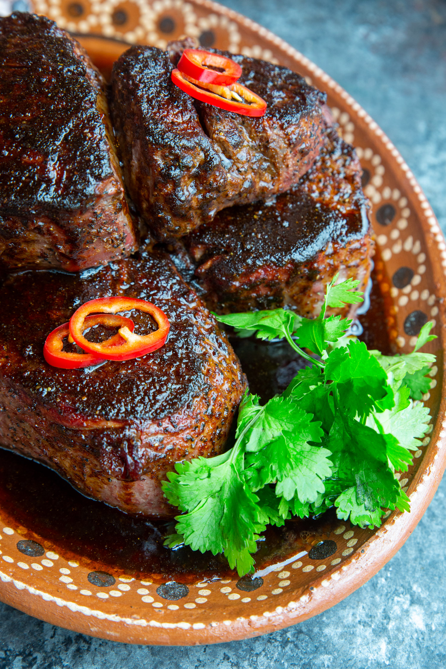 A platter full of steaks topped with mole butter, red peppers, and cilantro