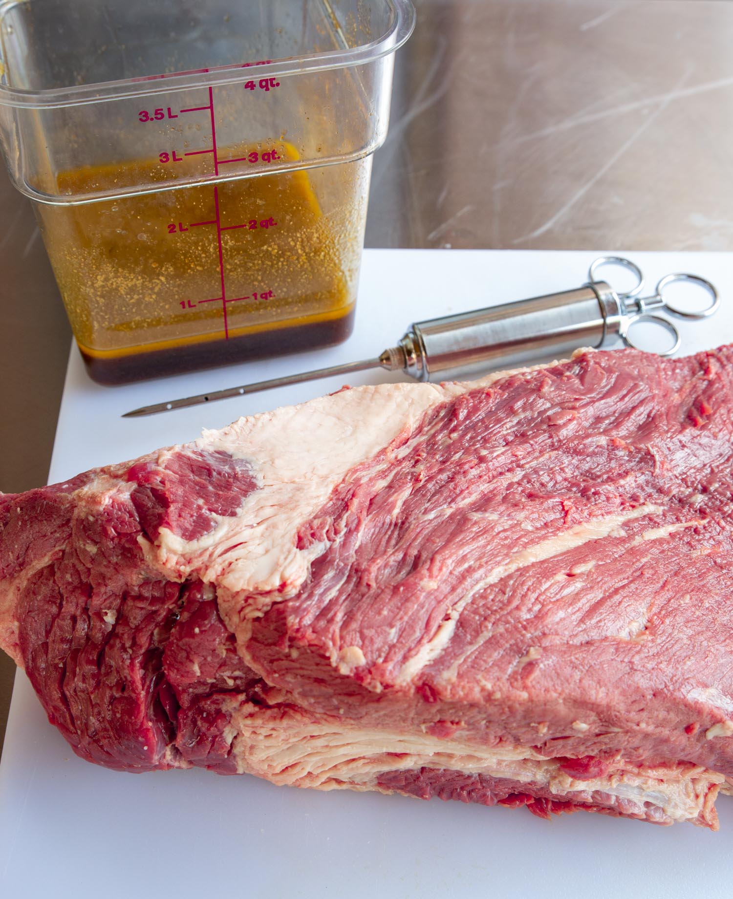 a brisket on a cutting board with the injector tool and the injection fluid.