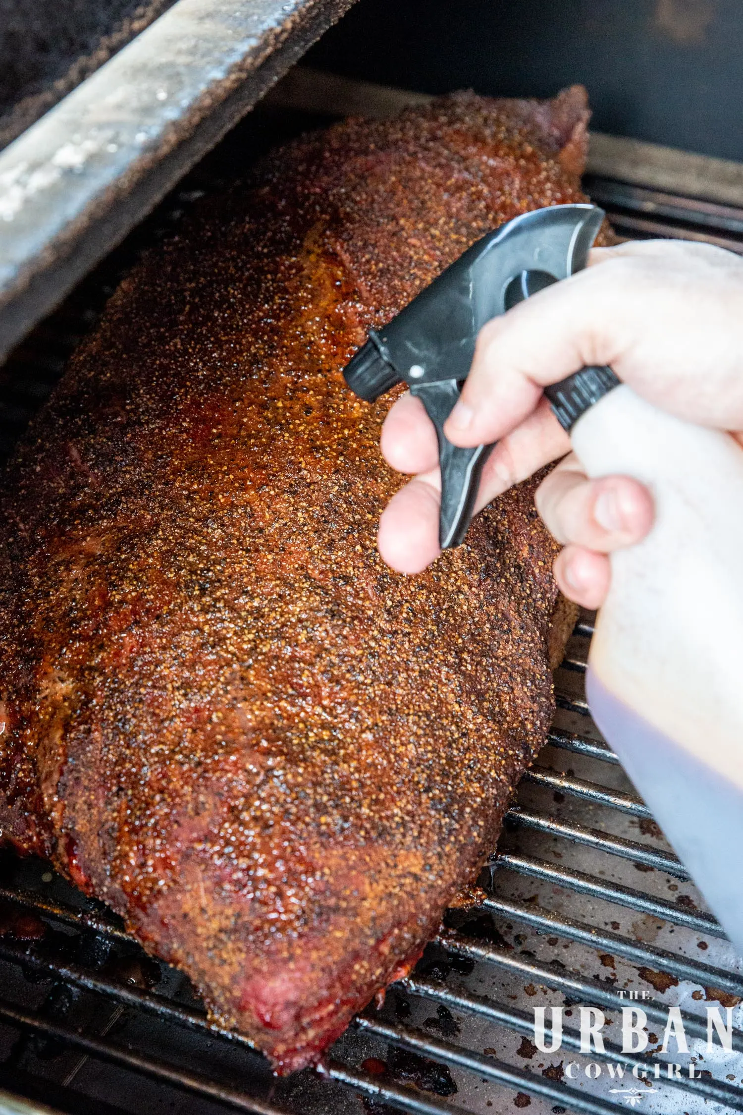 a brisket on the smoker being sprayed with a squirt bottle filled with red liquid.