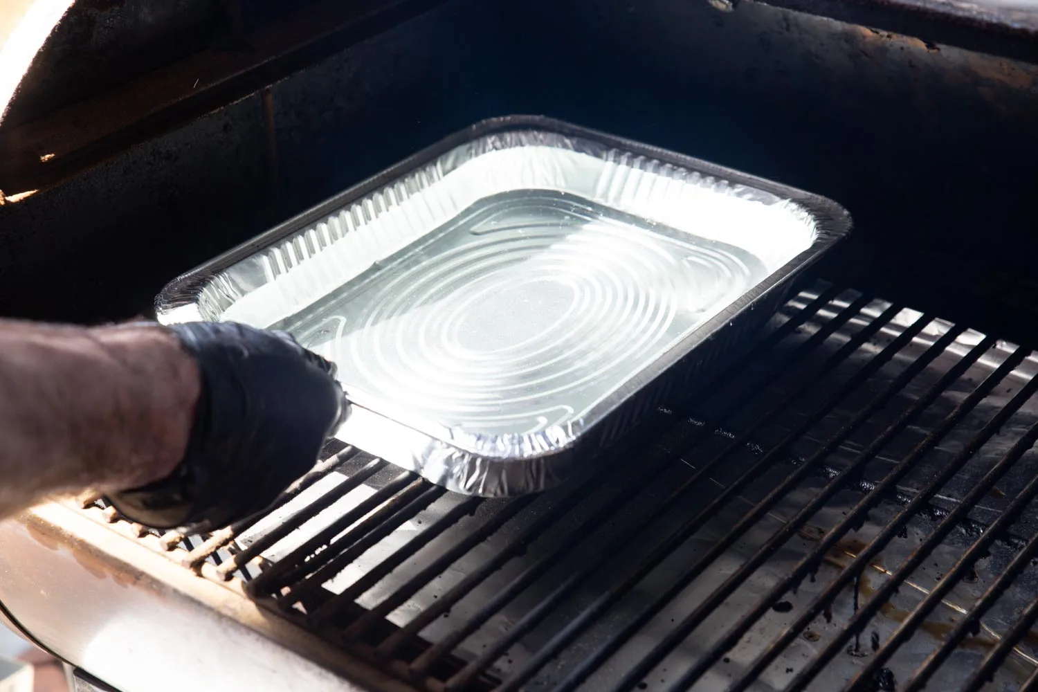 a man placing a water pan in the bbq smoker