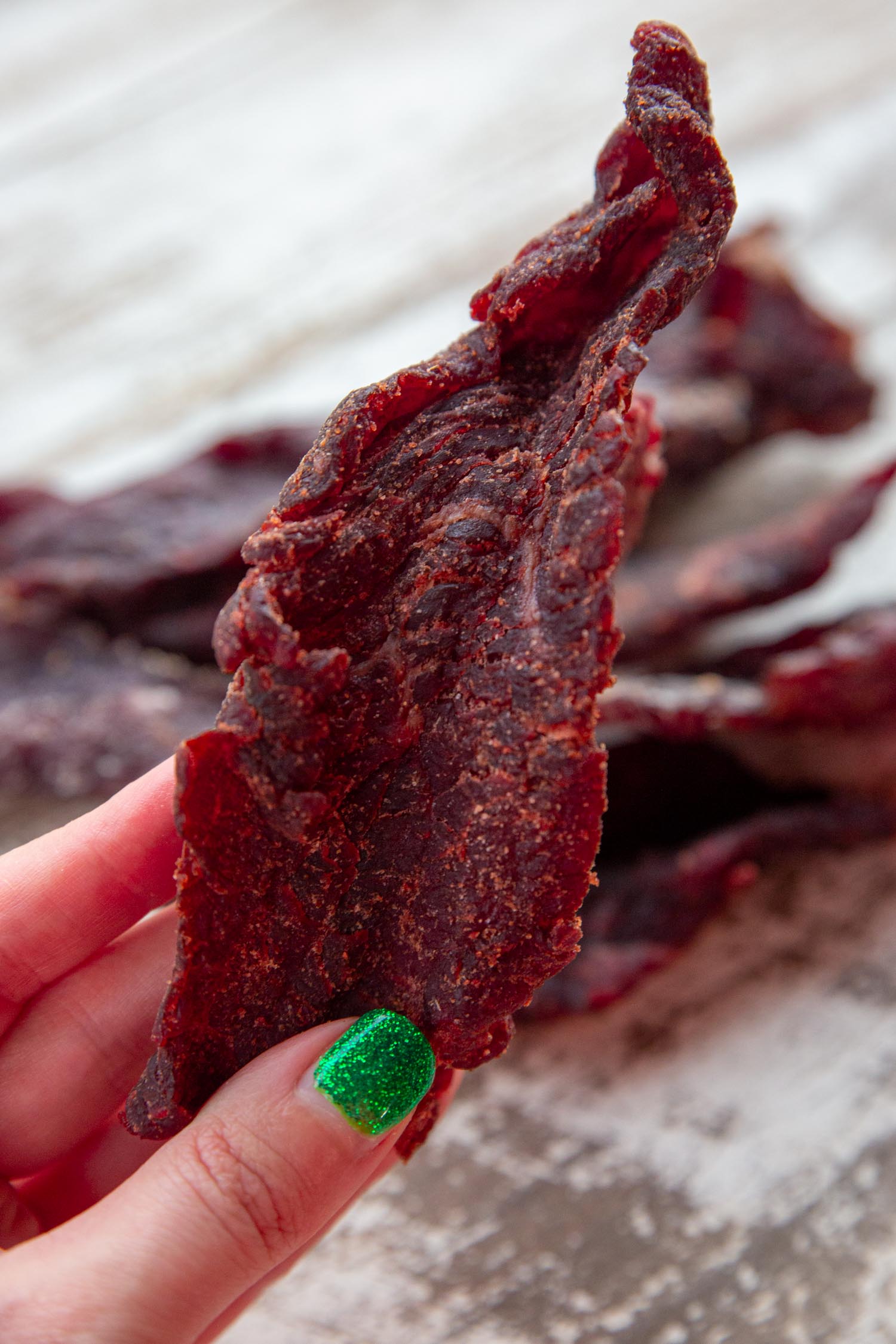 A hand holding up a piece of homemade beef jerky