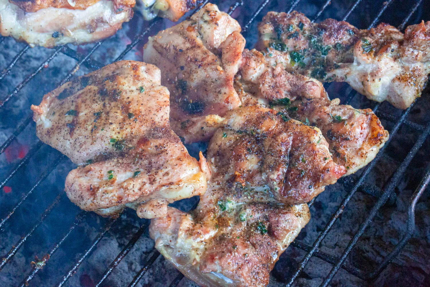 Boneless chicken thighs grilling over hot charcoal