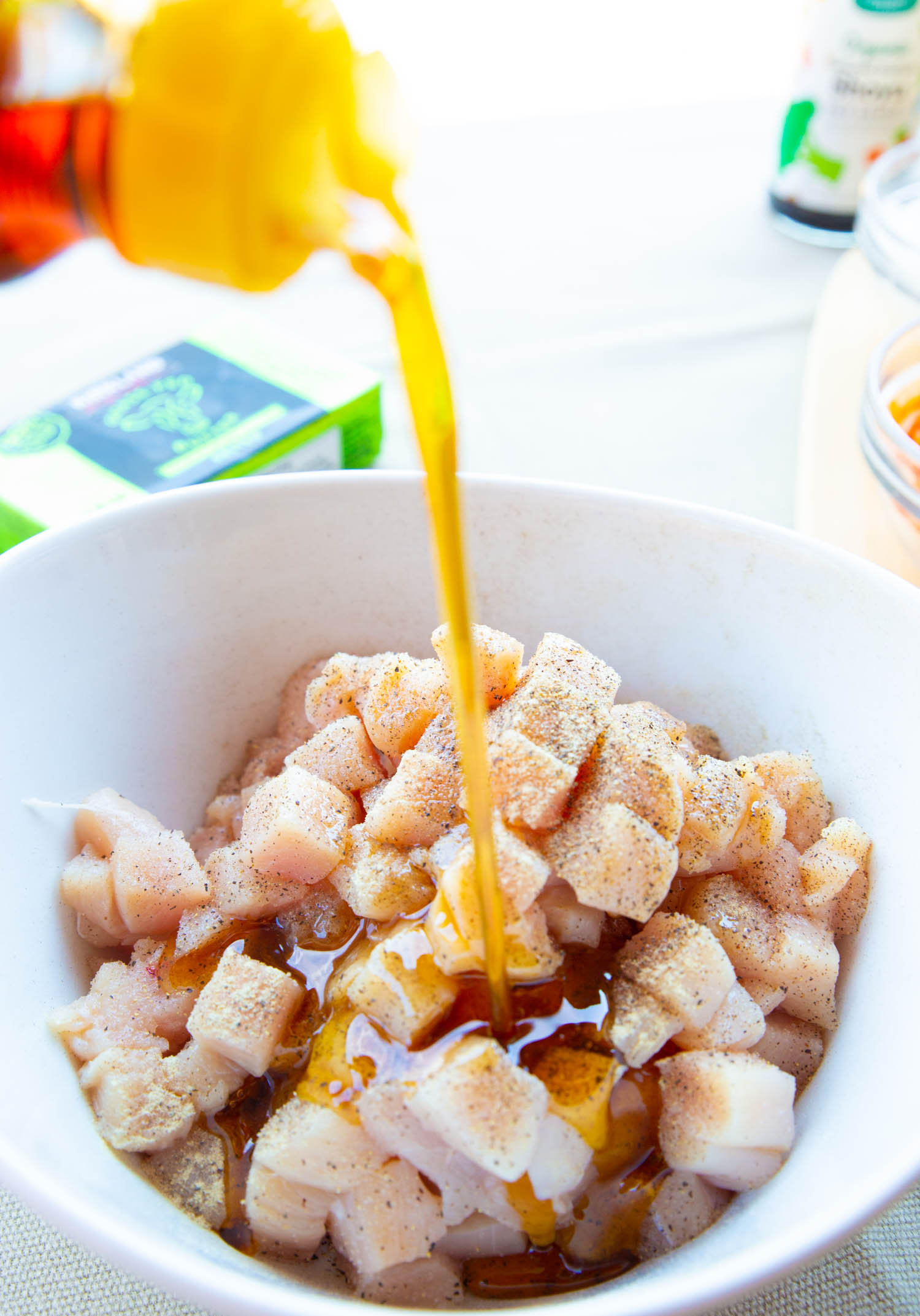 adding sesame oil to a bowl of diced chicken