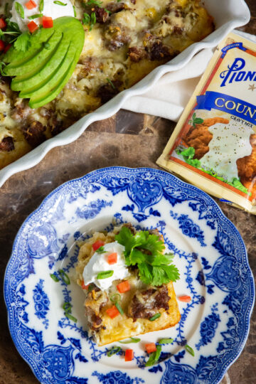 A blue plate of this sausage breakfast casserole topped with sour cream, tomatoes, and cilantro