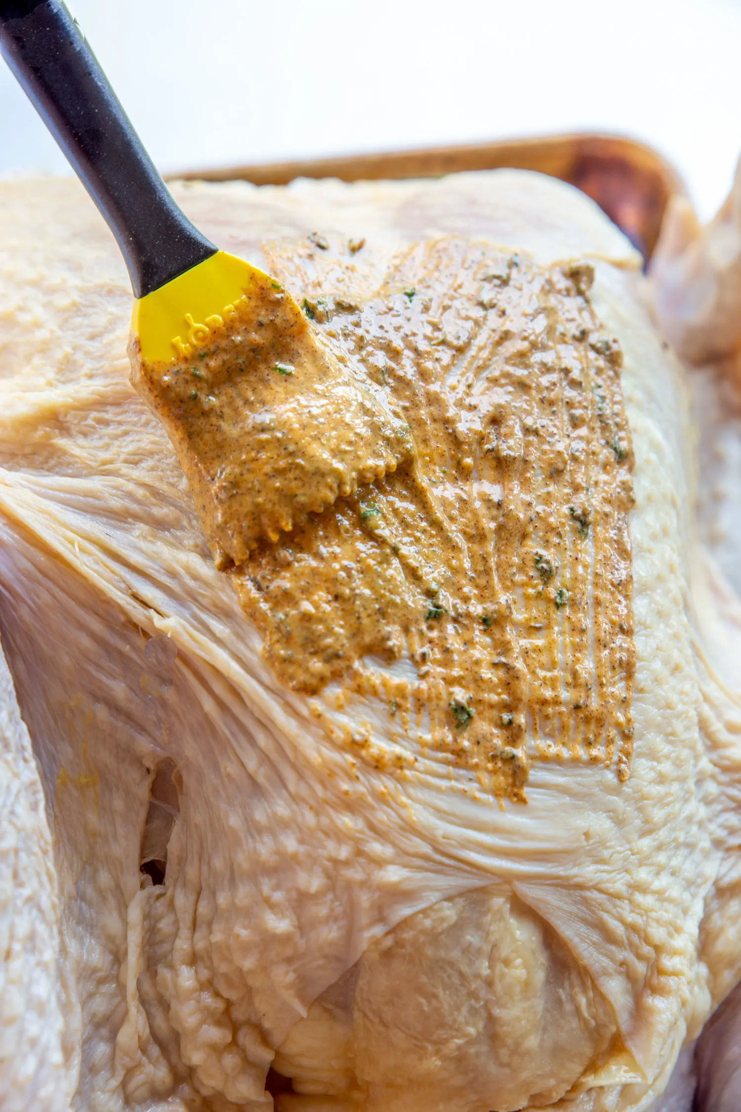 A raw turkey being painted with a silicone basting brush containing the turkey compound butter mixture.