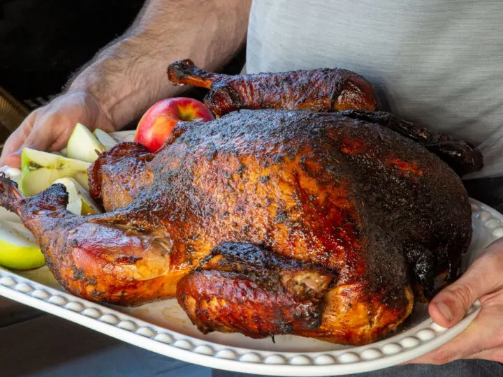 A man holding a whole smoked turkey next to a pellet grill