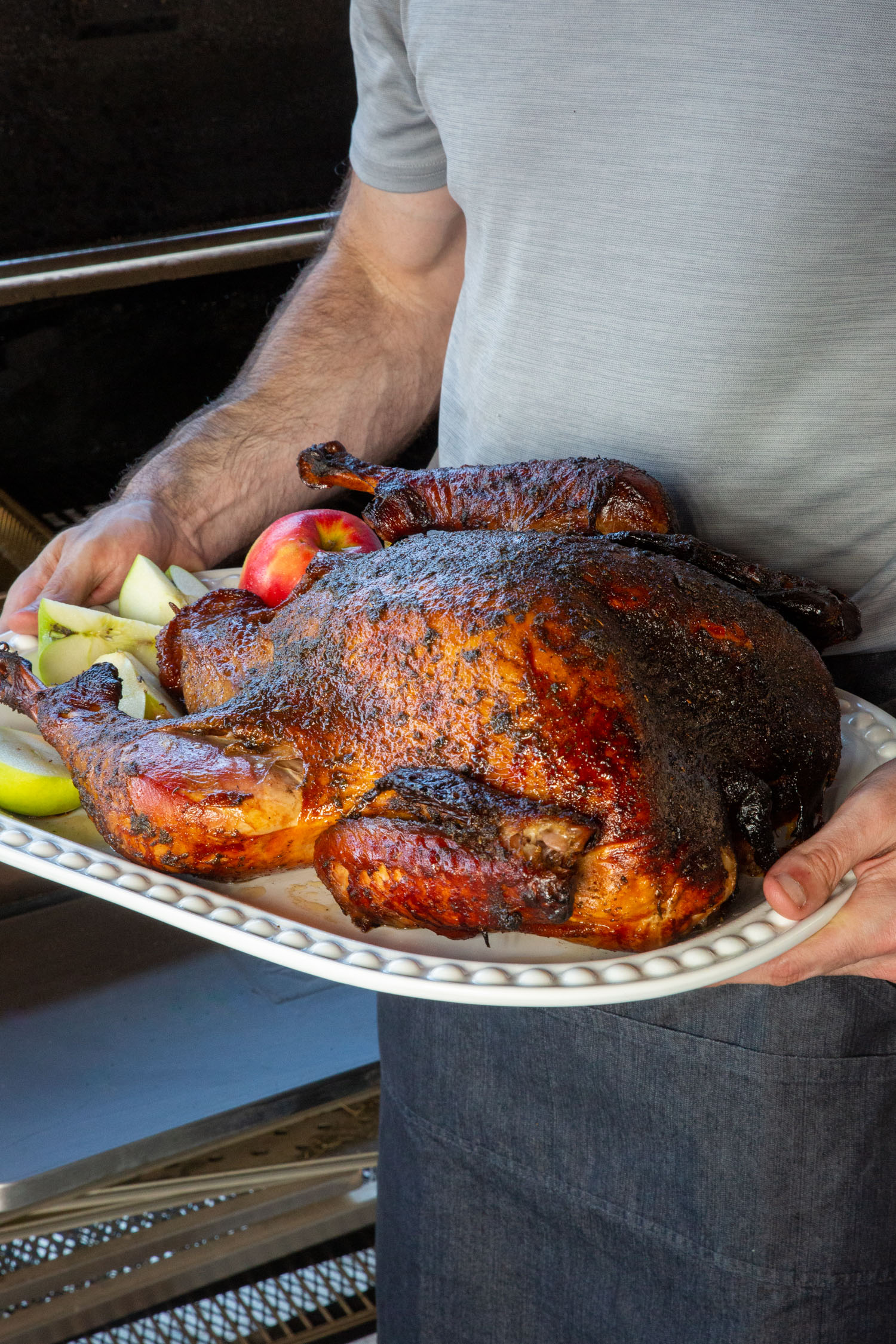 A man holding a whole smoked turkey next to a pellet grill