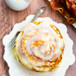 Cinnamon roll pancakes with icing and bacon on a wooden table.