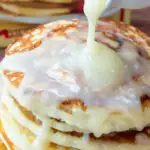 Pouring cream cheese drizzle on the pancakes.