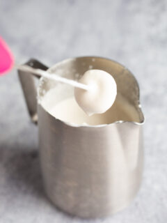 A milk frother in a stainless steel pitcher filled with soft top for coffee