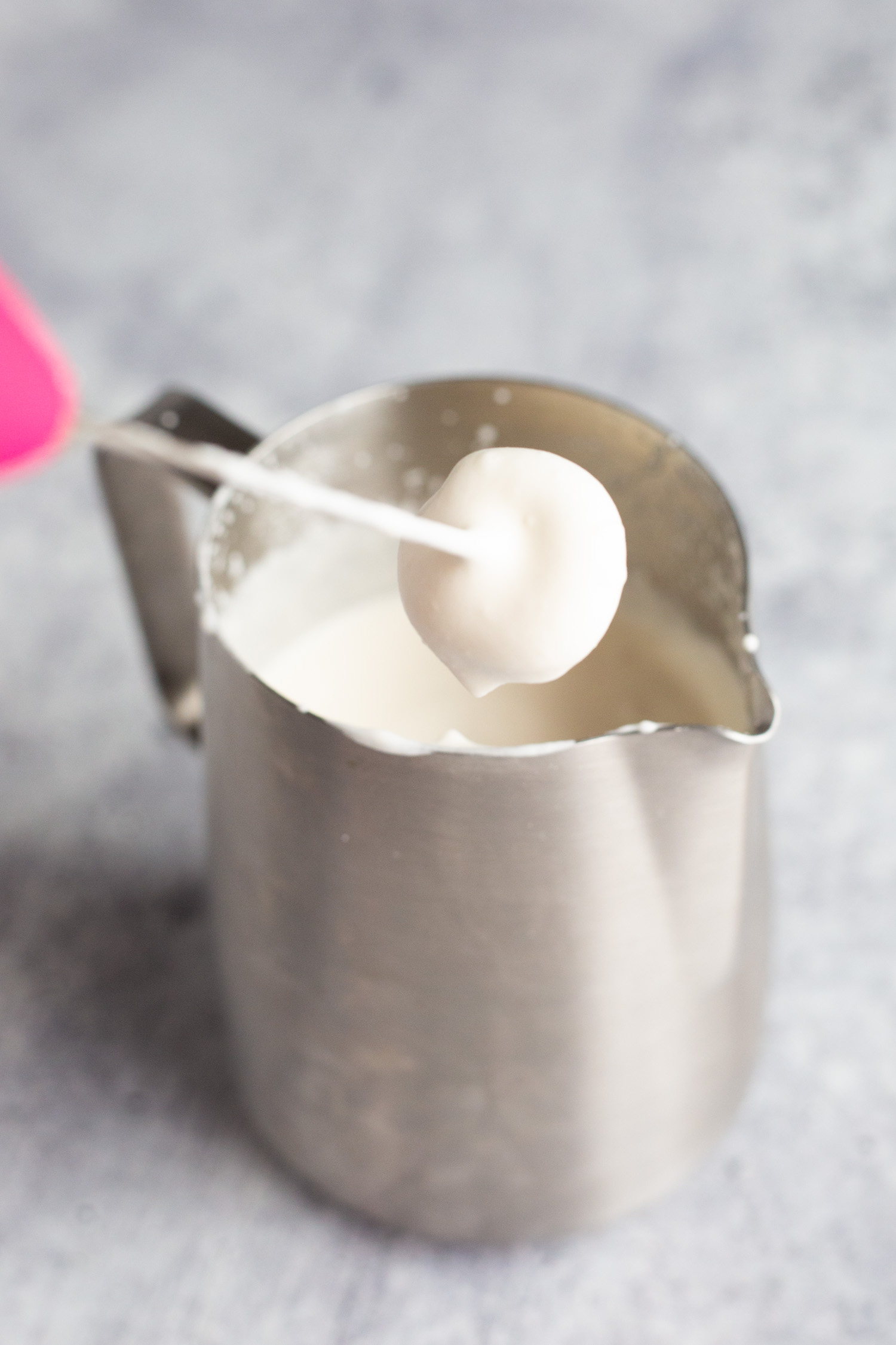 A milk frother in a stainless steel pitcher filled with soft top for coffee