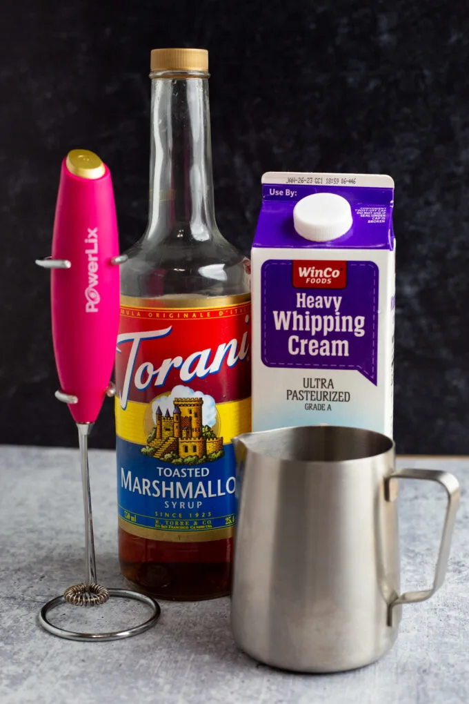 marshmallow syrup, cream, a milk frother, and a stainless steel cup for making the recipe