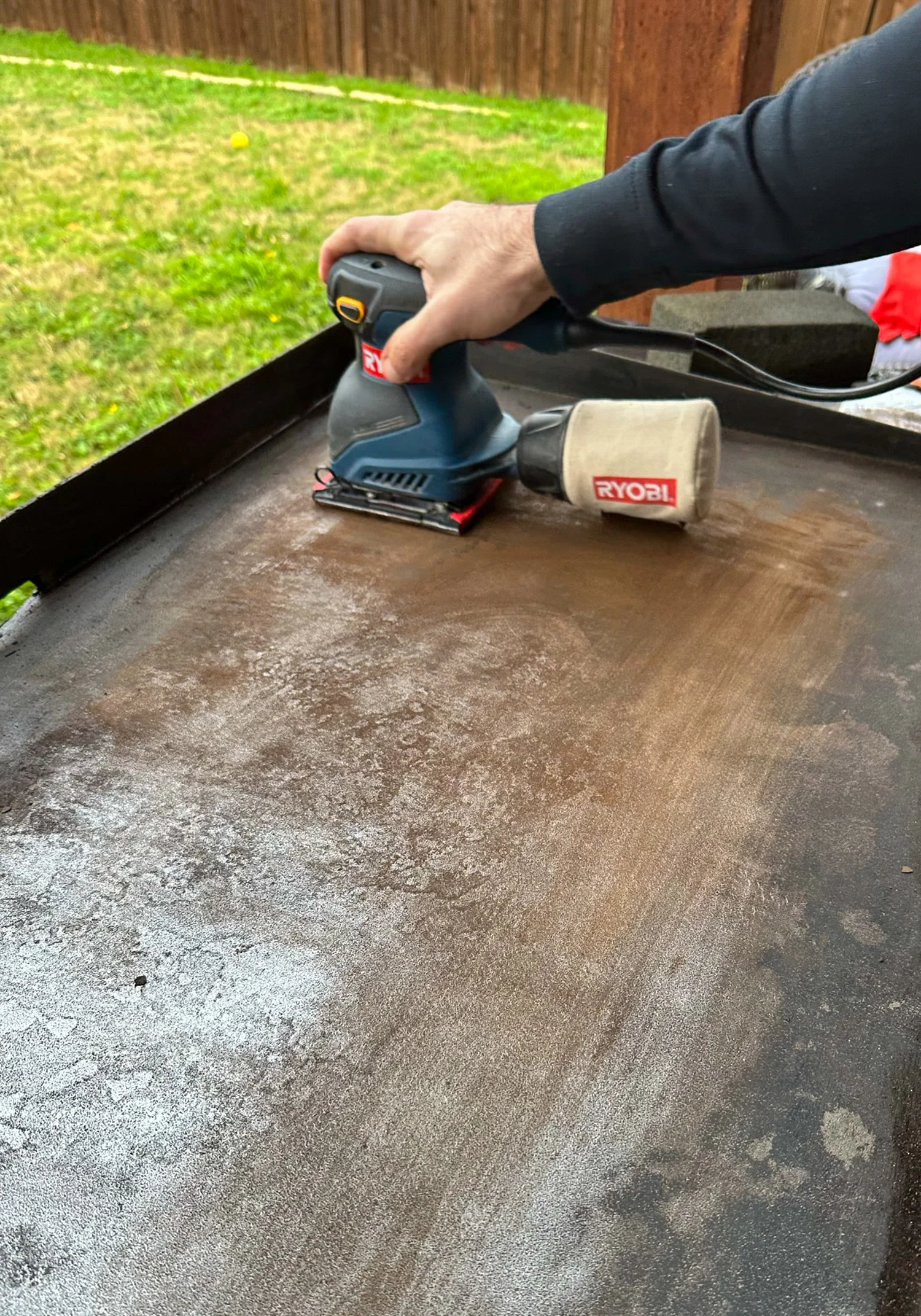 Sanding a griddle with a household sander to remove rust and debri.