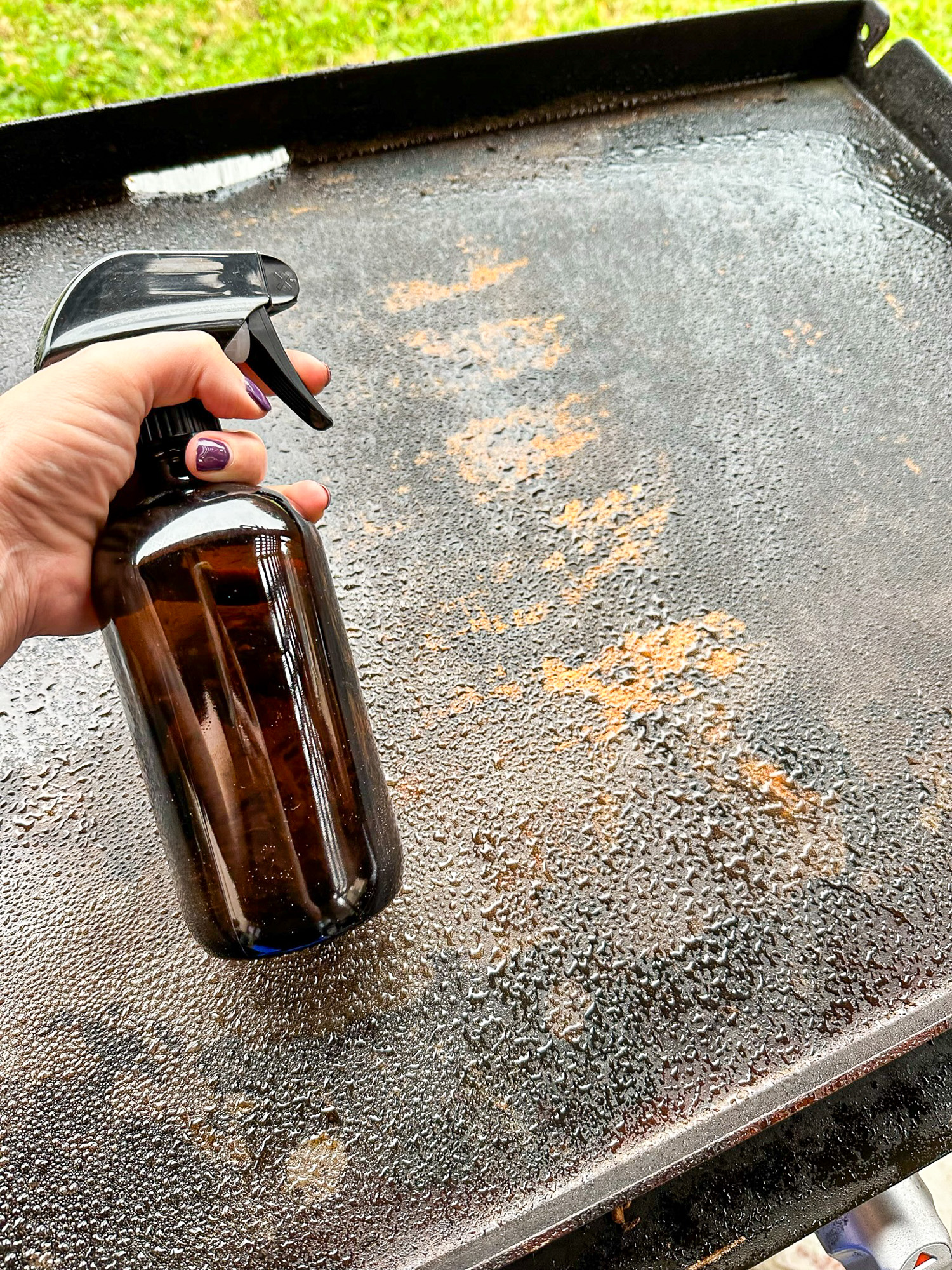 A rusted griddle sprayed lightly with vinegar from an amber spray bottle.