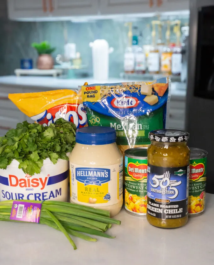 Ingredients for corn dip: sour cream, mayonnaise, cilantro, green onion, a jar of green chiles, and mexicorn.