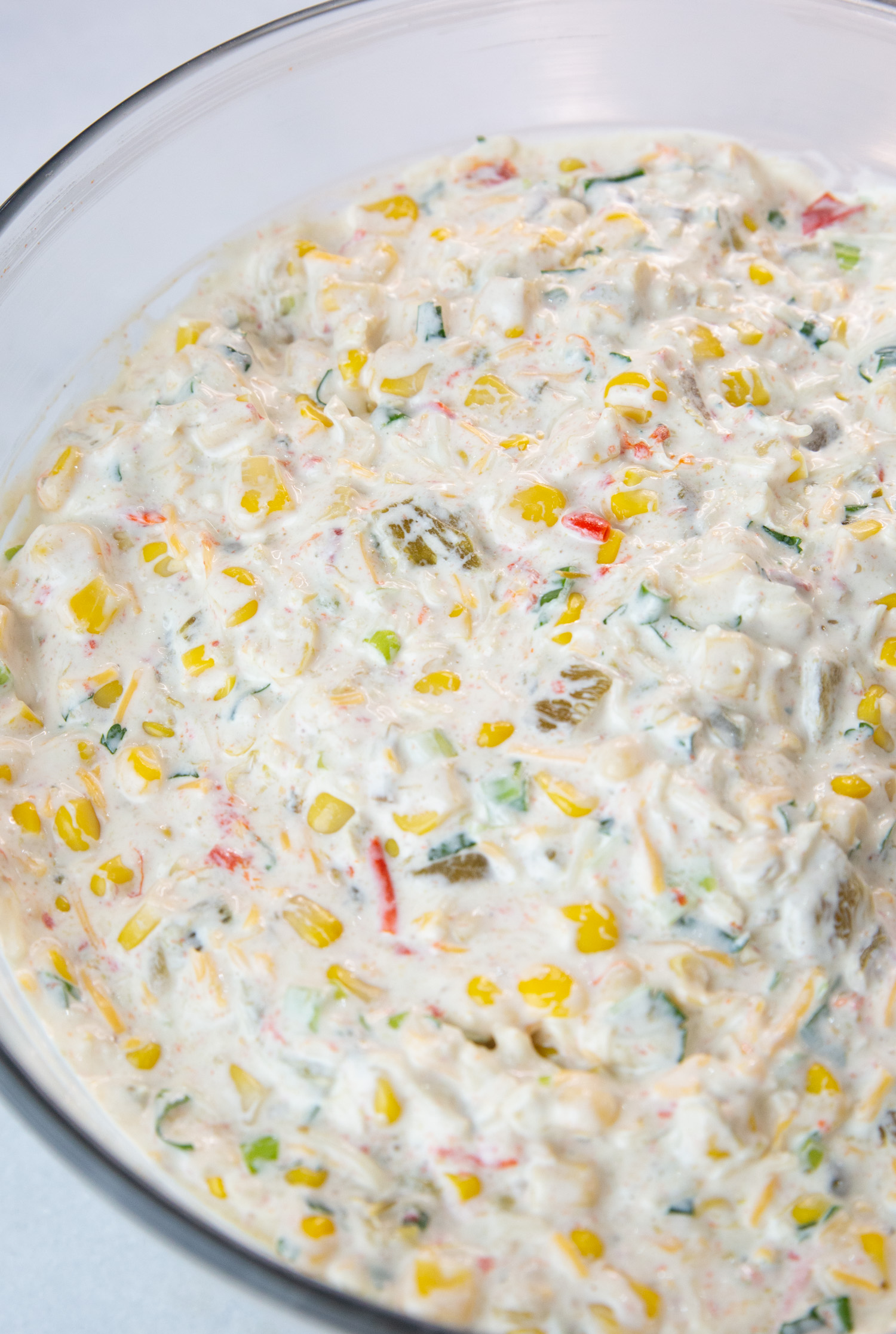 a bowl of freshly made corn dip with green chiles, jalapenos, sharp cheddar cheese, green onions, and cilantro.