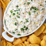 a bowl of corn dip surrounded by frito chips