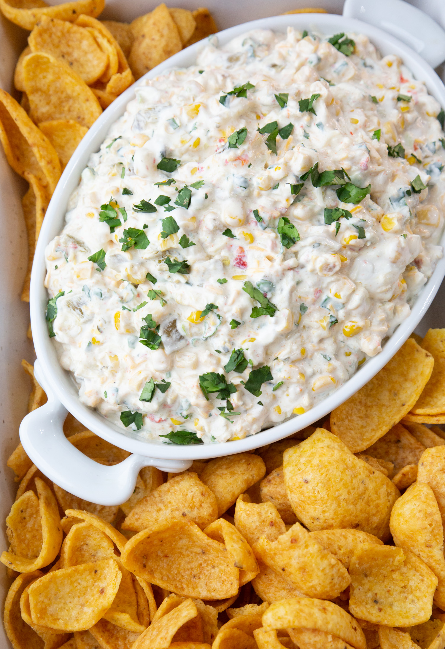 a bowl of corn dip surrounded by frito chips