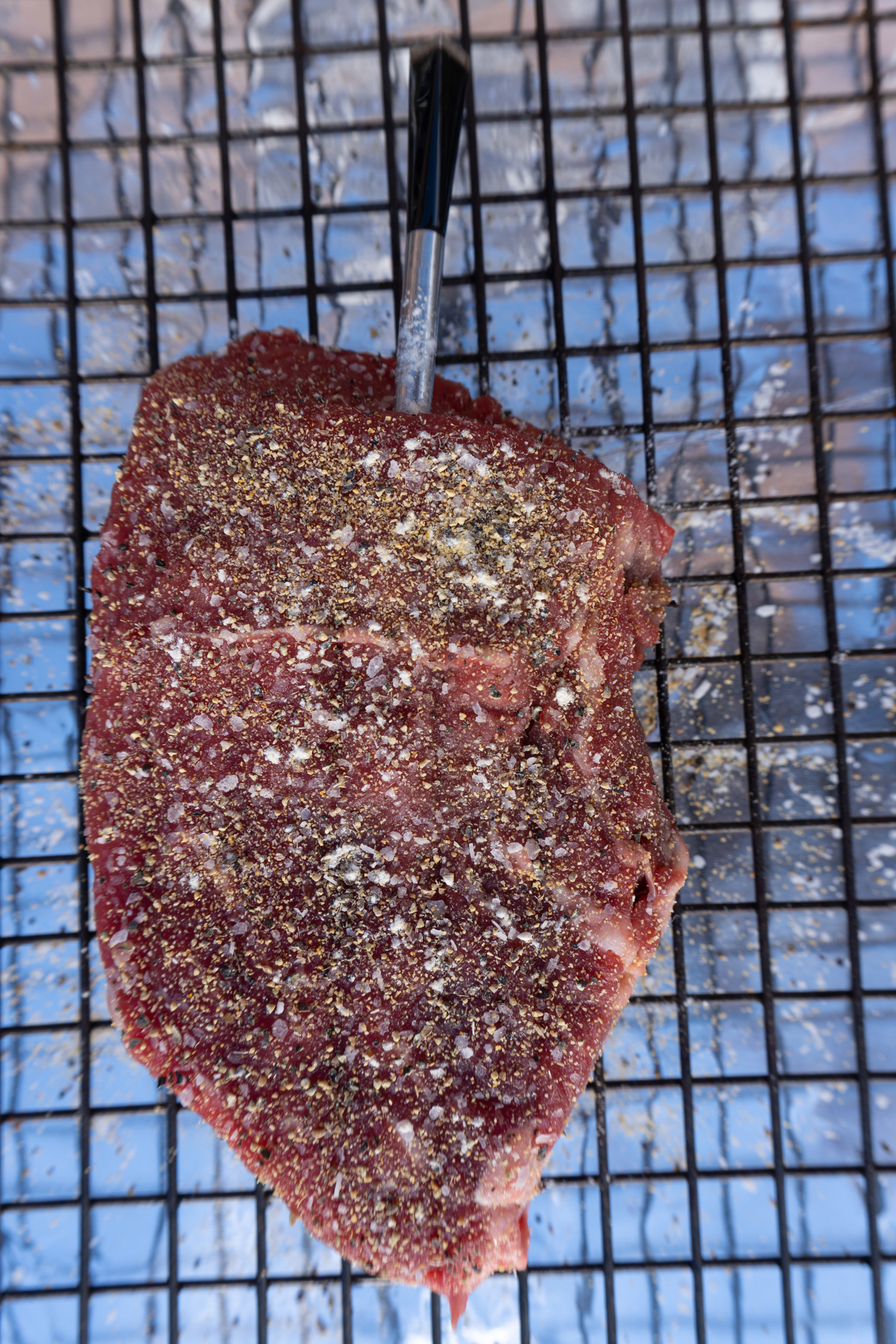 A raw steak with seasoning applied and probe inserted.