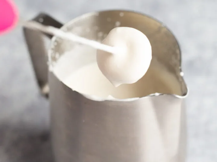 A stainless steel pitcher full of whipped cold foam with a milk frother.