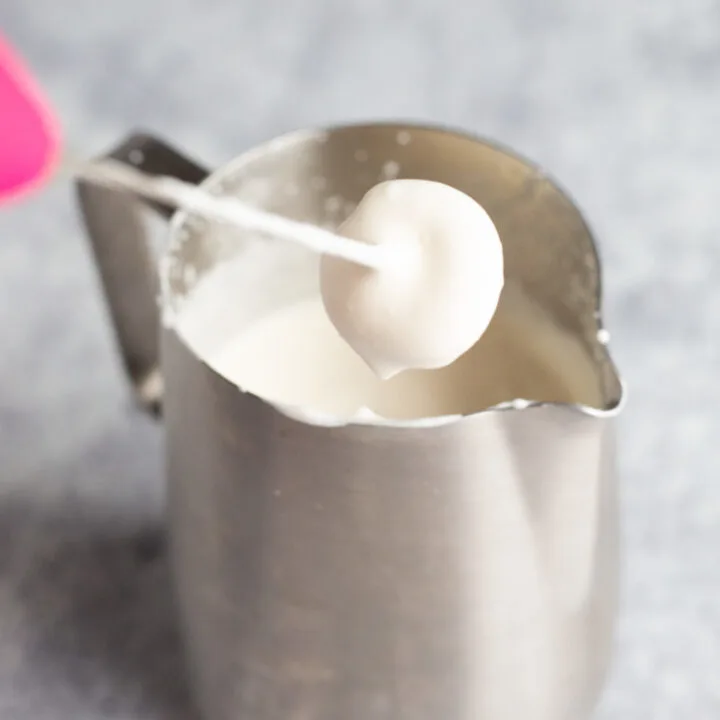 A stainless steel pitcher full of whipped cold foam with a milk frother.