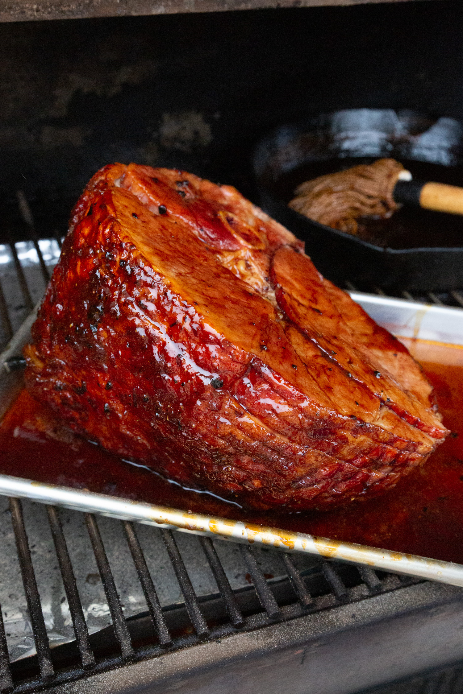 A smoked ham glazed with a bright red glaze sitting on a smoker.