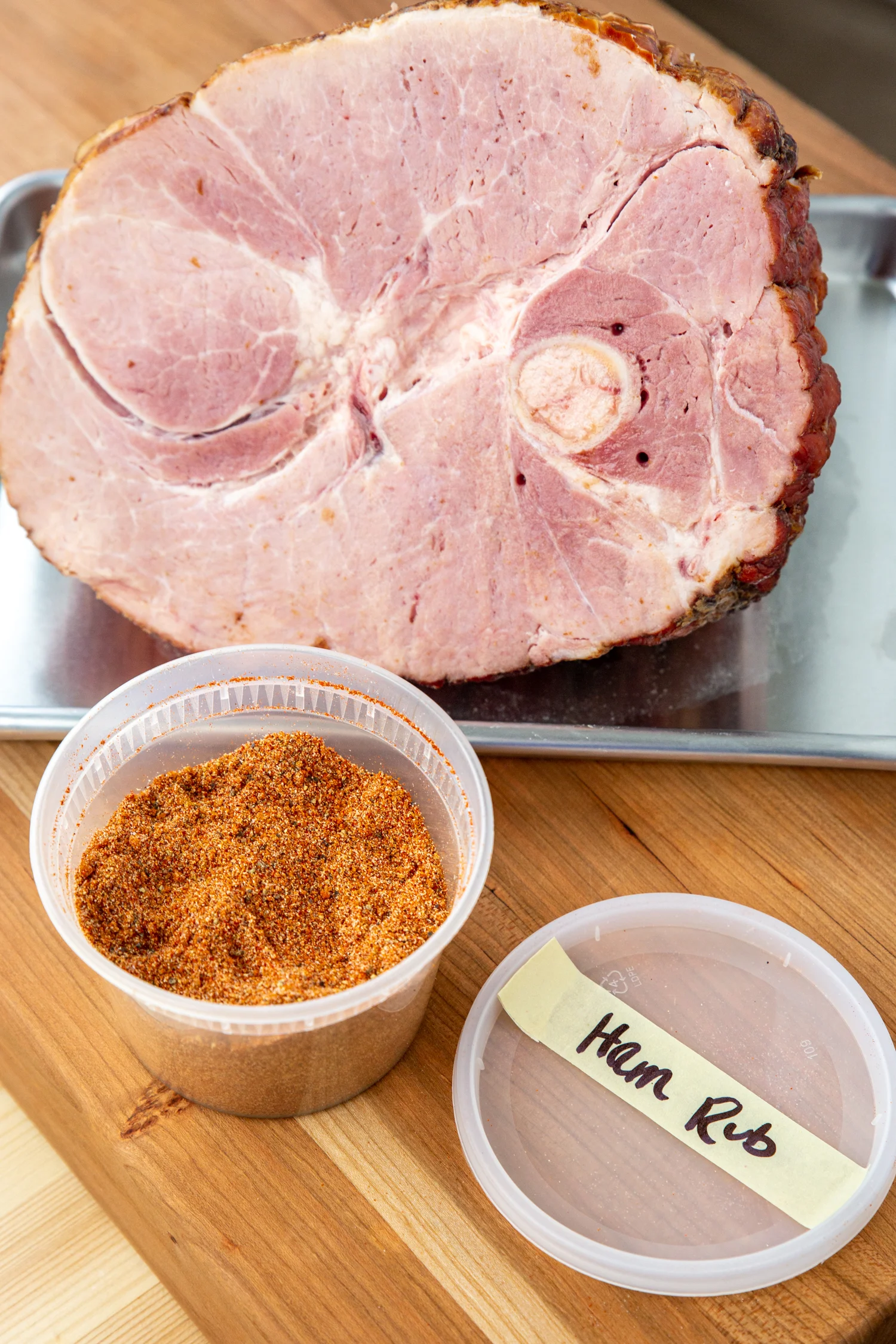The smoked ham rub in a container next to a raw ham.