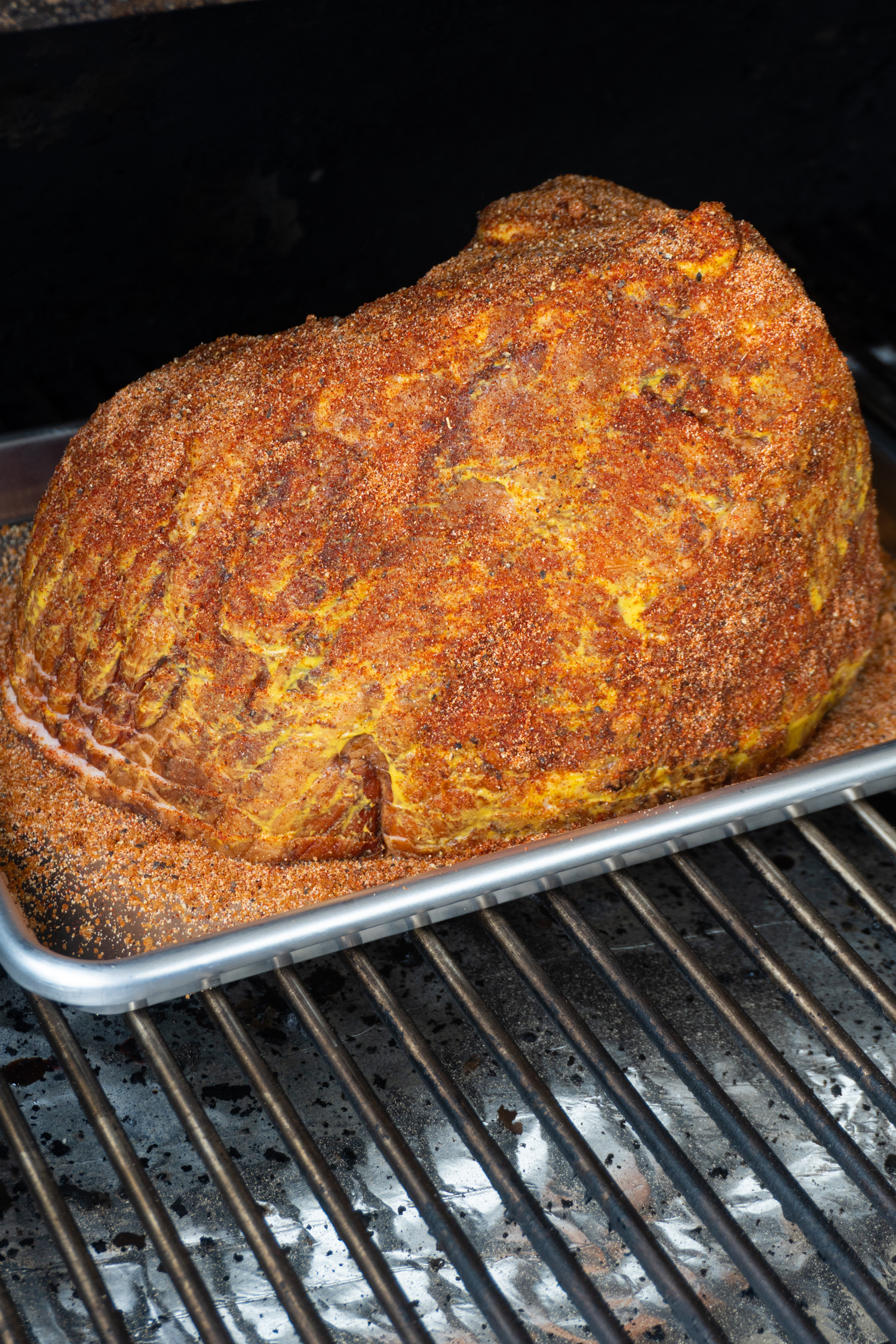 a raw ham on a barbecue smoker coated in dry rub.